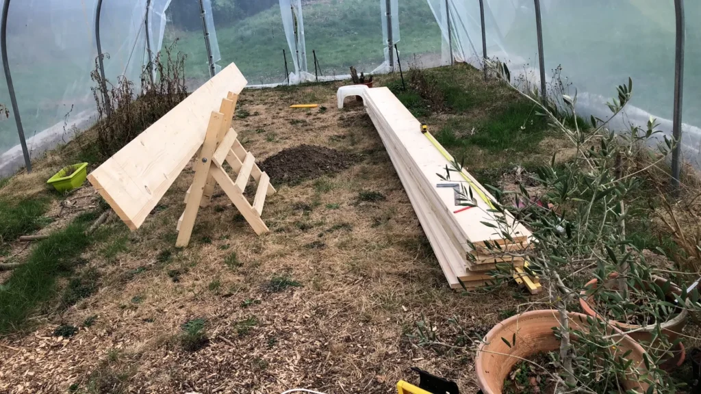 Planches de bois préparées pour la construction d’un carré potager surélevé dans une serre de jardin