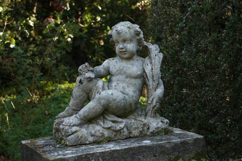 Sculpture en pierre représentant un enfant assis, intégrée dans un massif végétal au jardin de la Serre de la Madone, à Menton.