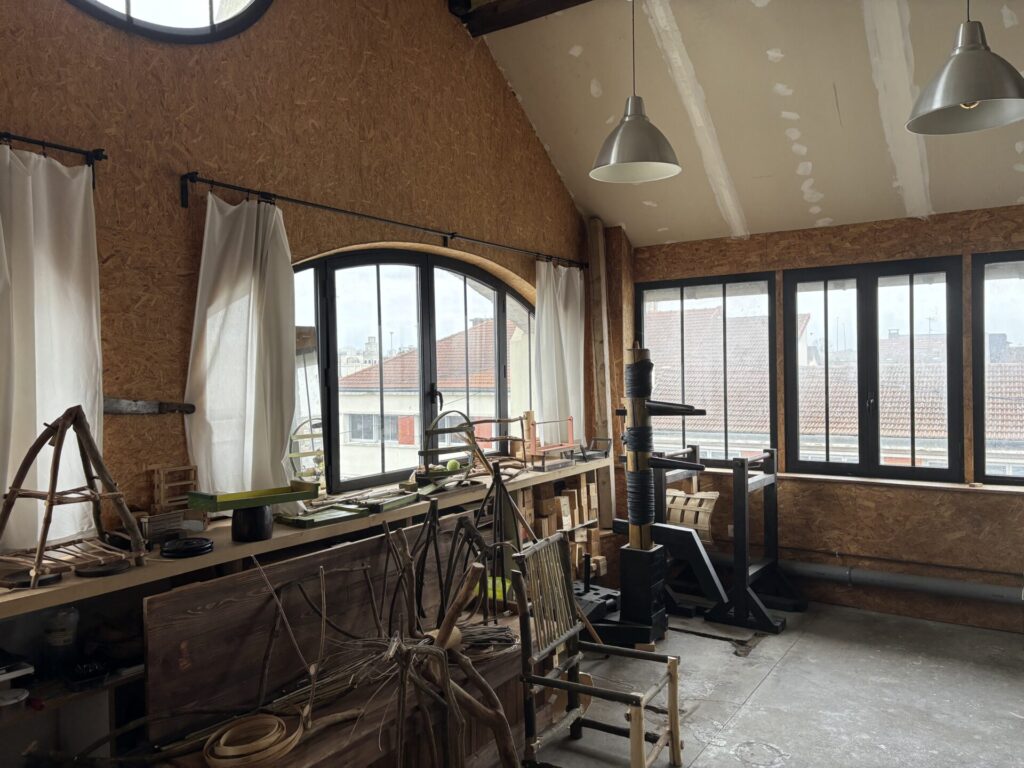 L’atelier d’Houman Ardalan avec des équipements et des créations artisanales en bois, éclairé par une lumière naturelle provenant de grandes fenêtres.