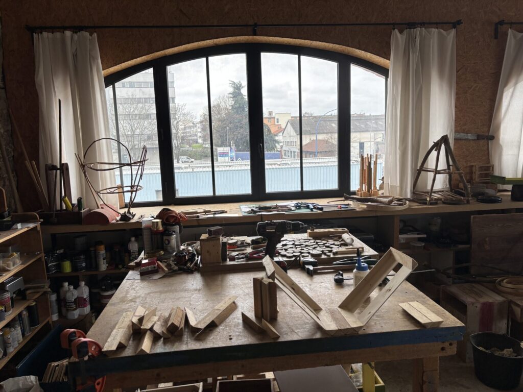 Vue intérieure de l’atelier d’Houman Ardalan, avec un établi en bois, des outils, et une grande fenêtre lumineuse donnant sur l’extérieur.