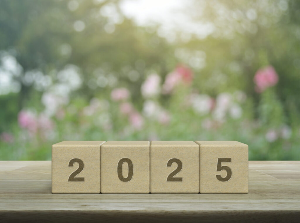Bloc en bois affichant 2025 sur une table avec un arrière-plan flou de jardin fleuri