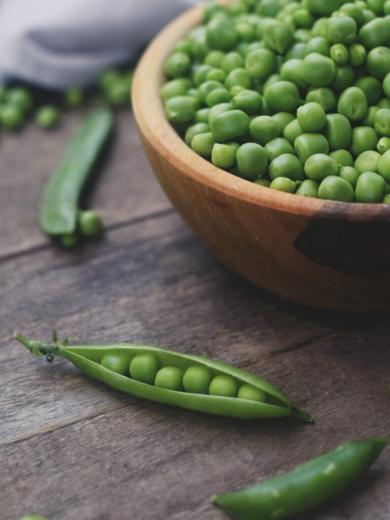Gros plan sur des petits pois verts frais, certains en gousse et d’autres dans un bol en bois, parfaits pour illustrer le jardinage ou la cuisine saisonnière.