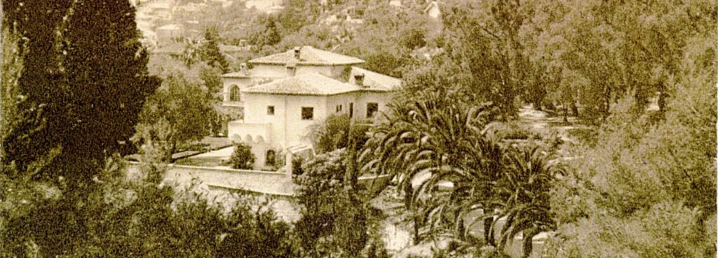 Vue ancienne du domaine de Val Rahmeh entouré de végétation méditerranéenne et exotique, avec une villa au style italo-provençal et des palmiers majestueux.