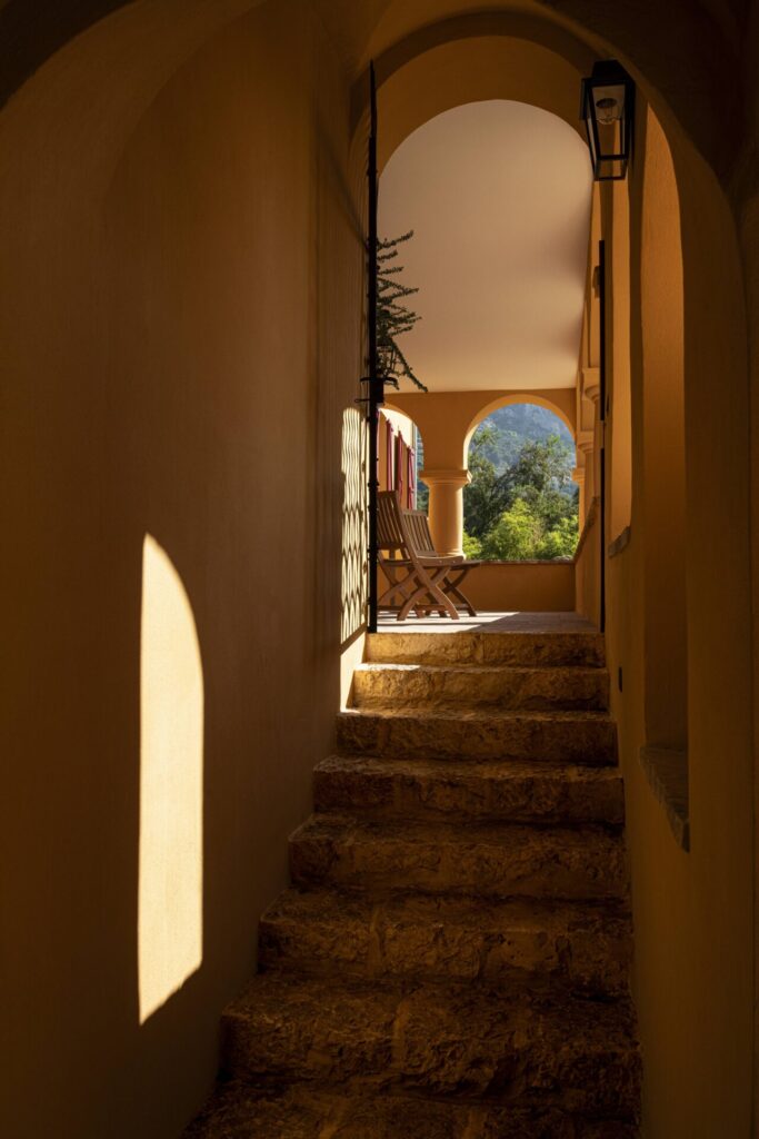 Escalier en pierre menant à une terrasse ombragée de la villa Val Rahmeh, Menton, avec une vue sur les montagnes environnantes.