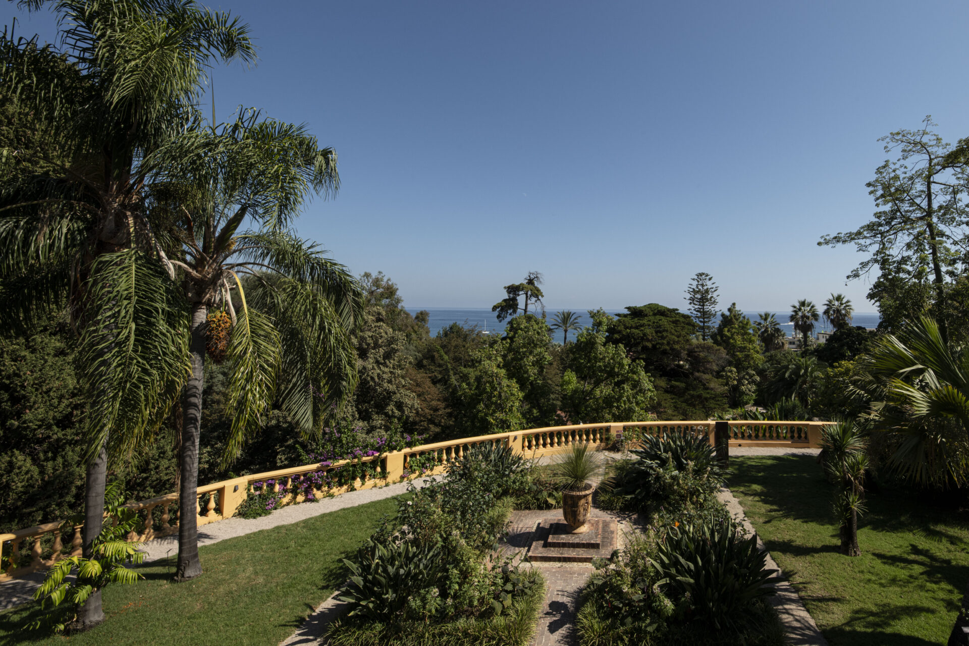 Vue sur la mer depuis le jardin de Val Rahmeh à Menton, entouré de palmiers et de plantes exotiques.