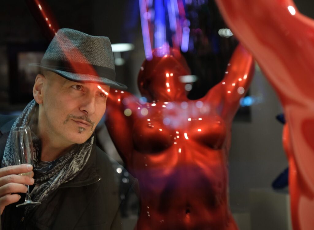 Yves Pires, sculpteur figuratif, contemplant l’une de ses œuvres en résine rouge lors d’une exposition, refletant sa vision artistique entre puissance et sensualité.