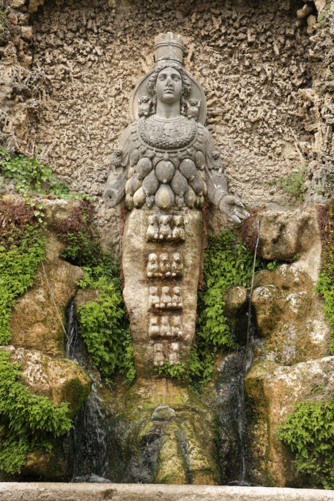 Statue de Diane d’Éphèse intégrée à une fontaine dans les jardins de la Villa d’Este à Tivoli, ornée de motifs symboliques.