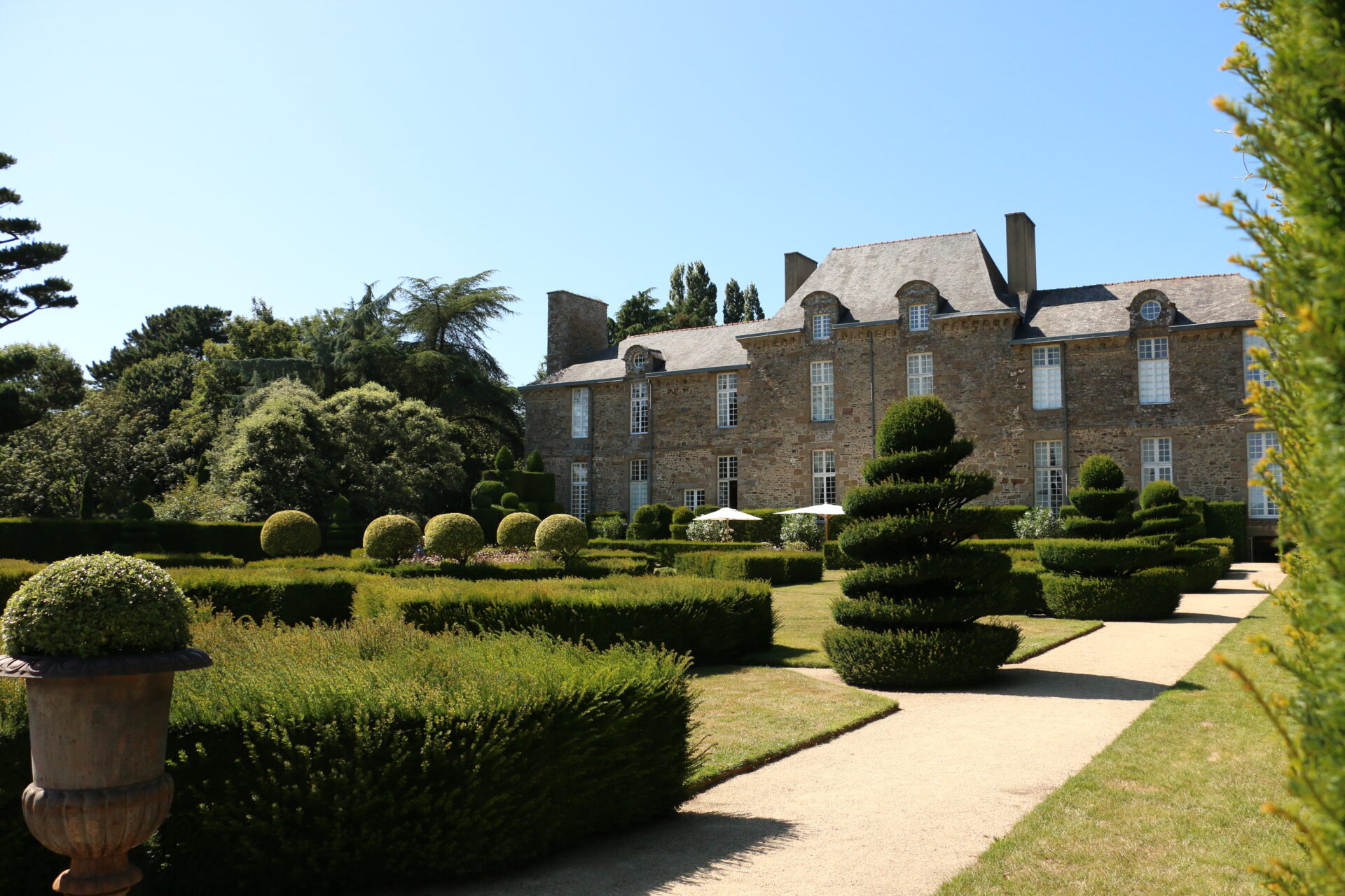 Terrasse sud du château de la Ballue, en Bretagne, bordée de topiaires, de buissons fleuris et d’un if pyramidal