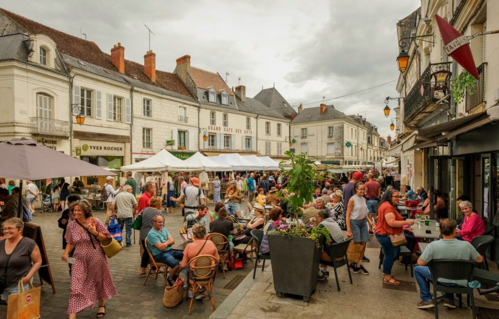 Scène animée du marché de Loches avec terrasses de café et étals de commerçants un jour d’été.