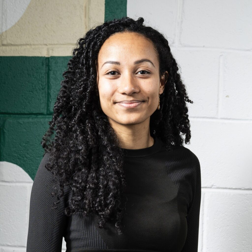 Charlotte Levif-Csösz en tenue noire, souriante, posant devant un mur blanc et vert