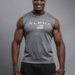 Portrait de Mamédy Doukhara, sportif, debout face à l’objectif, souriant, portant un débardeur gris sur fond neutre.